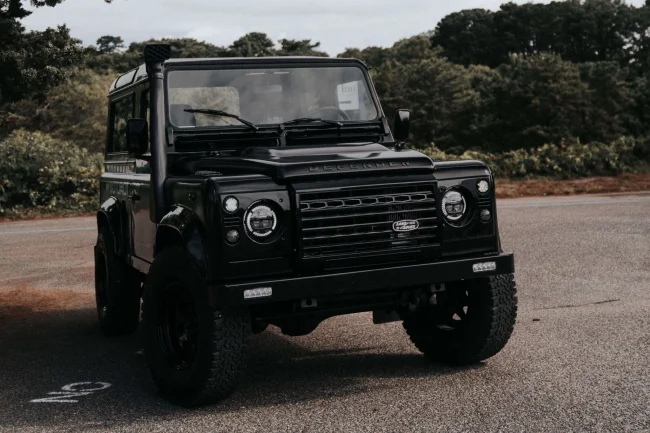A Satin and Matte Black Land Rover Defender 90 with LED lights and an LED bumper. The entire vehicle is blacked our or murdered out. This is an example of a custom and restored classic vehicle.