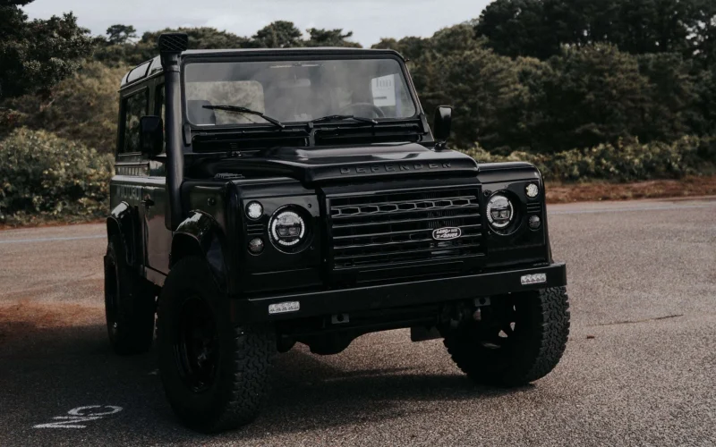A Satin and Matte Black Land Rover Defender 90 with LED lights and an LED bumper. The entire vehicle is blacked our or murdered out. This is an example of a custom and restored classic vehicle.